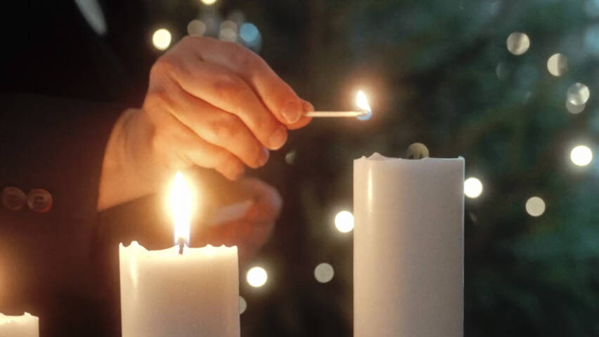 Kuvassa henkilön käsi, joka sytyttää kynttilöitä.