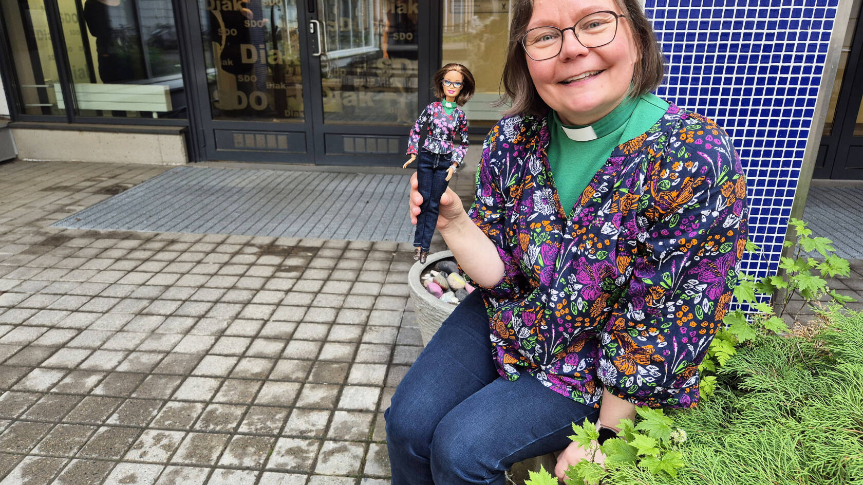 Pirita Satomaa istuu istutuksen vierellä kädessään Barbie-nukke.