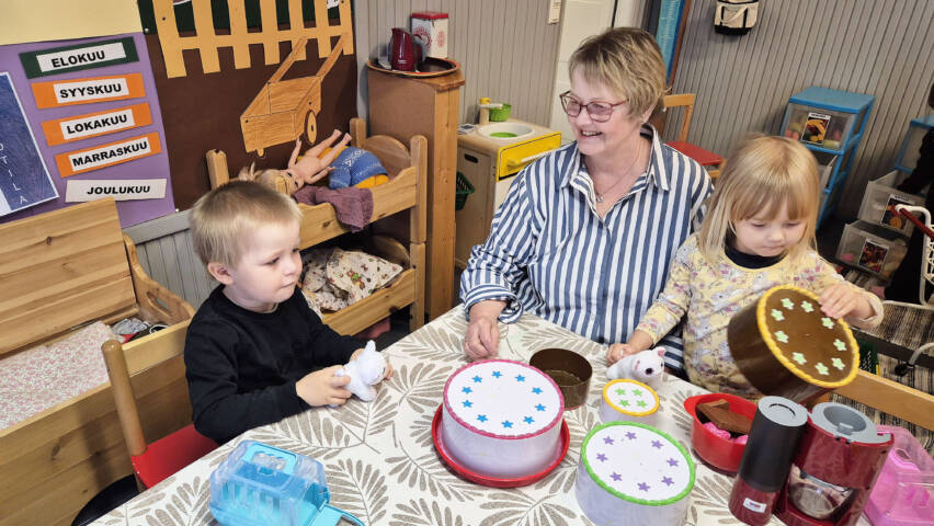 Henkilö istuu pöydän äärellä molemmilla puolilla leikkivä lapsi.